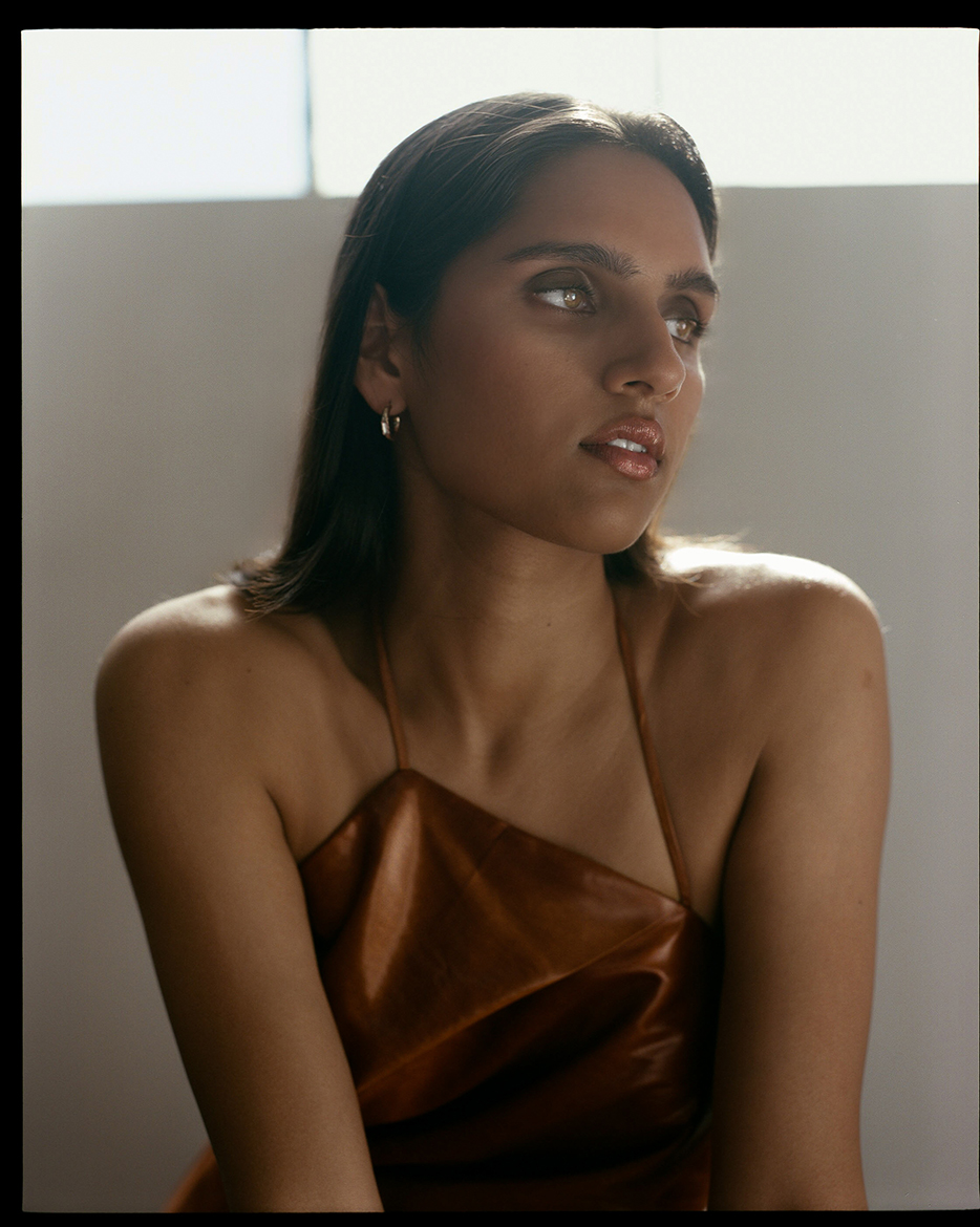 Portriat of a Model looking away from the camera with smokey eye makeup on wearing a copper colored top agianst a neutral background